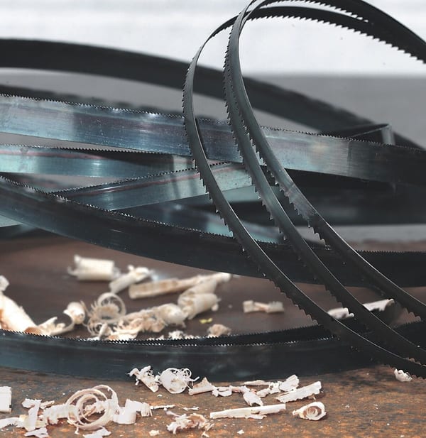 Metal bandsaw blades coiled on a surface with wood shavings scattered around, showcasing cutting tools and materials.